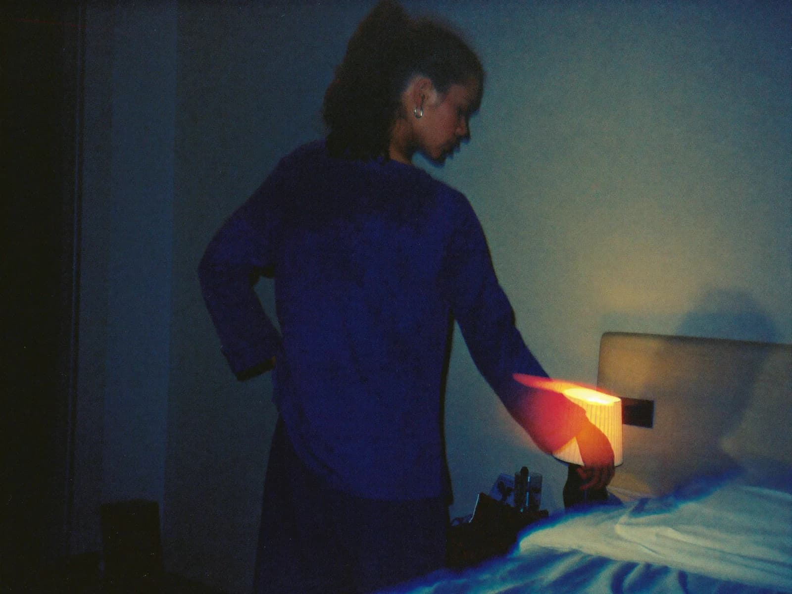 A woman reaching for a bedside lamp, photographed in soft blue light
